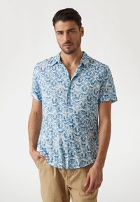 Camisa de manga corta en azul claro con un patrón geométrico blanco, con un cuello abotonado y una tela suave y transpirable.