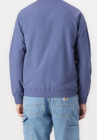 Navy blue jacket with elastic cuffs and hem, featuring a simple design and lightweight fabric. Worn over light blue cargo pants.