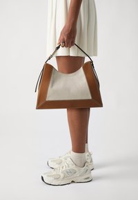Borsa marrone e beige con forma triangolare, bordi in pelle e corpo in tela, decorata con cuciture bianche e una tracolla corta.