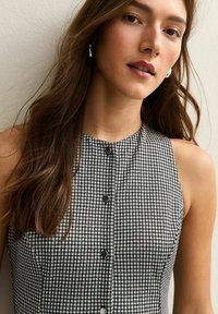 Abito senza maniche a motivo houndstooth in bianco e nero con scollatura alta e cinque bottoni neri centrati frontalmente. Tessuto dalla texture liscia.