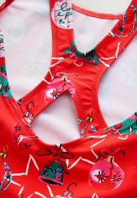Costume da bagno rosso con motivo di ornamenti colorati e fiocchi. Design incrociato sulla schiena con tessuto liscio ed elastico e rifiniture a contrasto.