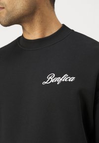 Sudadera negra con cuello redondo, que presenta texto bordado en blanco que dice "Benfica" en el pecho. Textura de tejido suave.