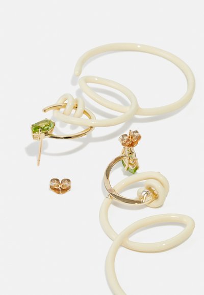 Los pendientes en tono dorado cuentan con un acento de piedra verde, un diseño retorcido en color marfil y formas circulares. Incluyen studs decorativos y elementos curvados.