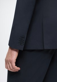 Marineblaue Anzugjackenmanschette mit vier schwarzen Knöpfen, taillierte Verarbeitung mit glatter Textur und schlanker, moderner Silhouette.