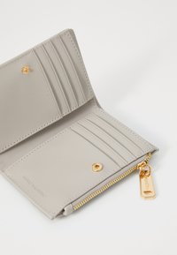 Portafoglio grigio chiaro con texture in pelle, multiple fessure per carte, un compartimento con zip, dettagli in metallo dorato e logo del brand in rilievo.
