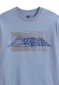 Lichtblauwe katoenen t-shirt met een grote, gestileerde grafiek in donkerblauw die een golf met een geblokt patroon en overlays in bruin toont.