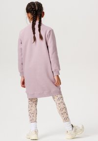 Lilla bomuldskjole med lange ærmer, parret med cremede blomstrede leggings og hvide sneakers. Struktureret stof og afslappet pasform.