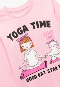 Roze katoenen T-shirt met een bedrukte afbeelding van een meisje en een kat die mediteren op yogamatten, met de tekst "YOGA TIJD" en "GOEDE DAG STAR."
