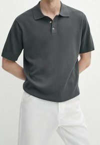 Polo shirt grigio scuro a maniche corte con tessuto texture, patta a tre bottoni e colletto classico, abbinato a pantaloni bianchi.