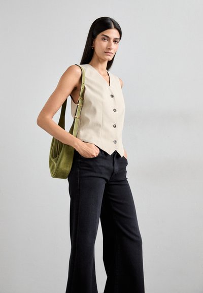Beige sleeveless button-up vest with a pointed hem, paired with black wide-leg pants. Model carries a green suede shoulder bag.