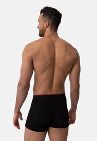 Svarta boxershorts med röd midjeresår, tillverkade i mjukt tyg, med en figurnära design och synliga sömmar.