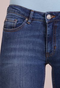 Mörkblå denimjeans har en klassisk femficksdesign, orange sömmar och en silverknäppning, vilket visar en mjuk yta.