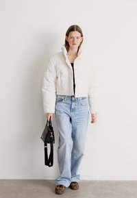 Fehér cropped pufikabát, fekete felső, világoskék farmernadrág és állatmintás cipők. Fekete kézitáska vállpánttal. Egyszerű, modern stílus.