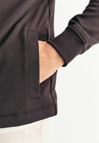 Must must have siled, mille tekstuuri, küljetasku ja soonikkoes varrukad. Üksikasjalik õmblusdetail allservas ja tasku serval.