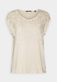 Krátký rukáv béžové tričko s kulatým výstřihem, zdobené jemným gradientem metalických zlatých skvrn na horní části. Měkká textura.