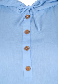 Helles blaues Oberteil mit Kapuze, gebundenem Ausschnitt und einer Knopfleiste mit braunen, runden Knöpfen an der Vorderseite. Glattes, strukturiertes Material.