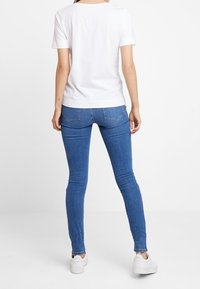 Camiseta blanca de algodón con mangas cortas combinada con unos vaqueros ajustados de denim azul. Los vaqueros tienen bolsillos traseros y detalles de costura sutiles.