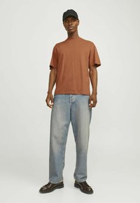 Brun kortærmet t-shirt, afslappet pasform, parret med løse lyseblå jeans og sorte sko. En sort kasket tilføjer et afslappet touch.