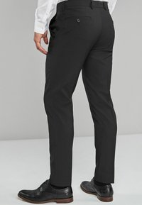 Zwarte op maat gemaakte broeken met een slim fit, voorzien van een gladde textuur, achterzakken en een knoopsluiting. Gecombineerd met zwarte veterschoenen.