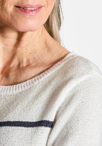 Lichtgekleurde gebreide trui met een ronde halslijn. Kenmerkt zich door een gestructureerd patroon en een donkere horizontale streep over het borstgebied.