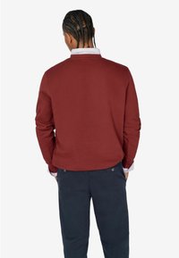 Burgunderfarbener Pullover mit langen Ärmeln und Rundhalsausschnitt, aus strukturiertem Strickstoff, kombiniert mit marineblauen Hosen. Sichtbare kontrastierende Kragen Details.