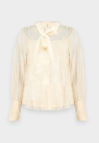 Ανοιχτό κρεμ μπλουζάκι από δαντέλα με λεπτομέρεια φιόγκου στο λαιμό, διάφανα μακριά μανίκια και μανσέτες με κουμπιά. Υφή με λουλουδένιο μοτίβο σε όλη την επιφάνεια.