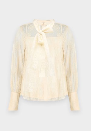 Vaalea kermanvärinen pitsipusero, jossa on rusetti kauluksessa, läpikuultavat pitkät hihat ja napilliset kalvosimet. Koko puseron läpi kulkee teksturoitu kukkakuvio.