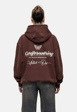 Bruine cropped hoodie met een witte afdrukte afbeelding van een vlinder en tekst op de achterkant. Zachte stof, verstelbare capuchon en een losse fit.