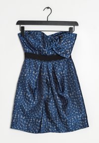 Olkaimeton tummansininen satiinimekko, jossa on hunajakennokuvio. Mekossa on solmittu yksityiskohta ylhäällä ja musta vyötäröosa.