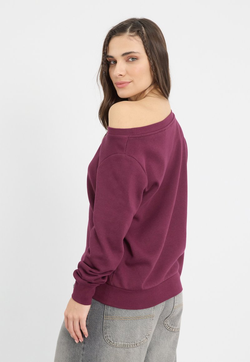 Burgundowa bluza z odkrytymi ramionami, z długimi rękawami i prążkowanymi mankietami, w połączeniu z jasnoszarymi spodniami typu high-waisted, o minimalistycznym designie.