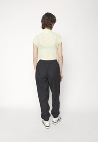 Camisa corta de color amarillo claro con un diseño texturizado, combinada con pantalones negros de cintura elástica y zapatillas blancas con acentos amarillos.