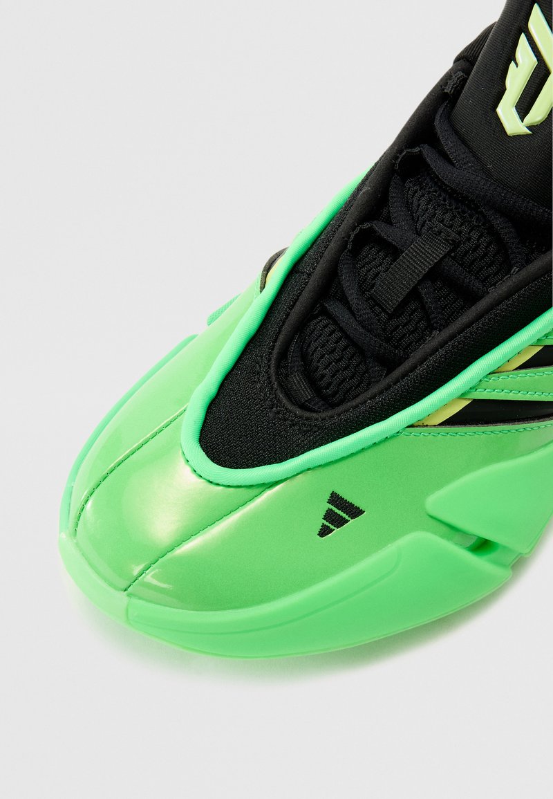 Scarpa sportiva verde con una parte superiore lucida e liscia, dettagli in rete nera, sistema di lacci e un distintivo logo nero sul lato.
