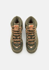 Zapatillas altas en color verde oliva con forro de piel texturizada, detalles en naranja y cordones con estampado. Presentan una puntera reforzada y un cuello acolchado.