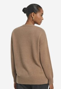 Brauner Pullover mit geripptem Saum und Manschetten, im entspannten Schnitt und mit Rundhalsausschnitt. Die Textur wirkt weich und gestrickt.