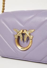 Mala de mão em pele lilás com acolchoamento em padrão chevron, apresentando um fecho em tom dourado na forma de dois pássaros. Corrente incluída.