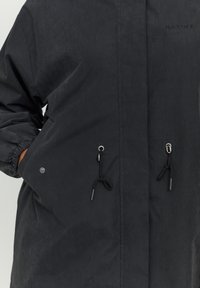 Czarna kurtka z kapturem z detalem ze sznurkiem na dole, wyposażona w elastyczne mankiety i przednie kieszenie. Materiał ma matową fakturę.