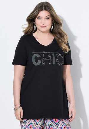 T-shirt noir à manches courtes en V avec le texte "Forever CHIC" orné de strass. Porté avec un pantalon coloré à motifs.