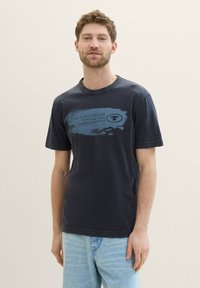 Mørkeblå bomulds t-shirt med rund hals og korte ærmer, prydet med et grafisk print i lyseblå tekst og abstrakt design på forsiden.