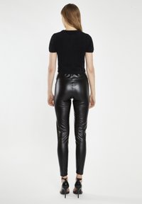 Top corto nero in pelliccia sintetica a maniche corte abbinato a leggings finti in pelle lucida neri a vita alta, caratterizzati da una vestibilità slim e una lunghezza alla caviglia.