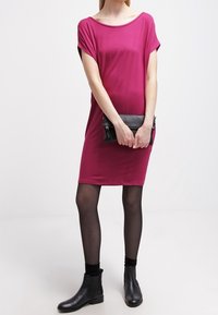 Fuchsia short-sleeved dress with a loose fit, paired with black ankle boots and a black clutch. The fabric appears smooth and stretchy.