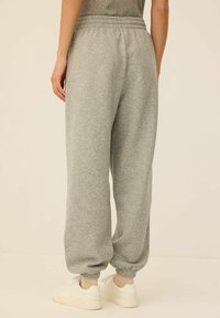 Szare dresy z elastycznym paskiem w talii, zakończone ściągaczami, o miękkiej fakturze. Stylizowane w luźnym kroju, zestawione z białymi sneakersami.