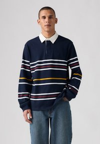 Polo de manga larga en color marino con cuello blanco, con franjas horizontales en rojo, blanco y amarillo. Tejido suave y texturizado.