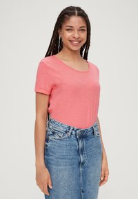 T-shirt à manches courtes et col arrondi en tissu rose clair, associé à une jupe en denim taille haute. Texture douce, coupe décontractée.