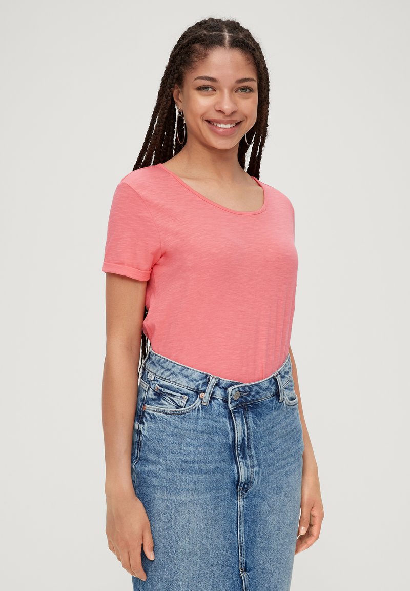 T-shirt à manches courtes et col arrondi en tissu rose clair, associé à une jupe en denim taille haute. Texture douce, coupe décontractée.