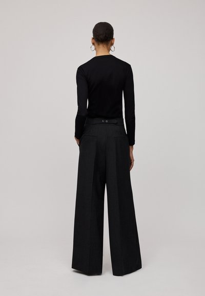 Top negru cu mâneci lungi, cu un design ajustat, asortat cu pantaloni gri cu talie înaltă și picior larg, prevăzuți cu un închidere cu nasture la spate și buzunare.