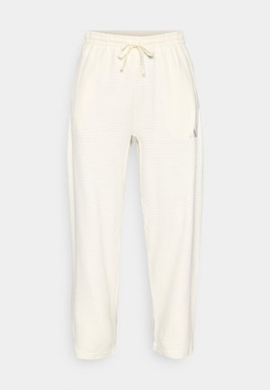 Pantalones deportivos de color crema claro, hechos de una tela texturizada, que cuentan con una cinturilla elástica con cordón y bolsillos laterales.