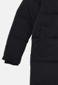 Manteau doudoune navy avec des manches présentant des détails de couture horizontale et un poignet élastique. Comprend une poche sur le bras supérieur. Texture lisse.