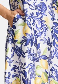 Ein blumenmusterndes Gewebe mit lebhaften blauen und gelben Zitronen auf einem weißen Hintergrund, mit sichtbarem Taschen an der Seite. Glatte Textur.