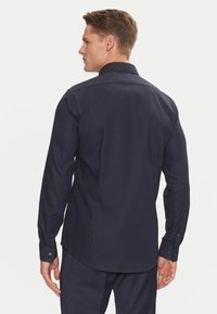 Camicia navy a maniche lunghe con bottoni, realizzata in un tessuto testurizzato, con orlo curvo e polsini con bottone, vista da dietro, che mette in evidenza la vestibilità e il design.