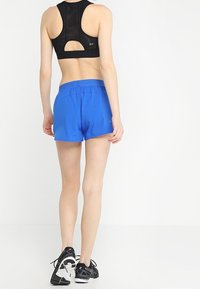 Svart sportbh med skärning; livliga blå shorts med elastisk midja; svarta träningsskor med vita accenter.